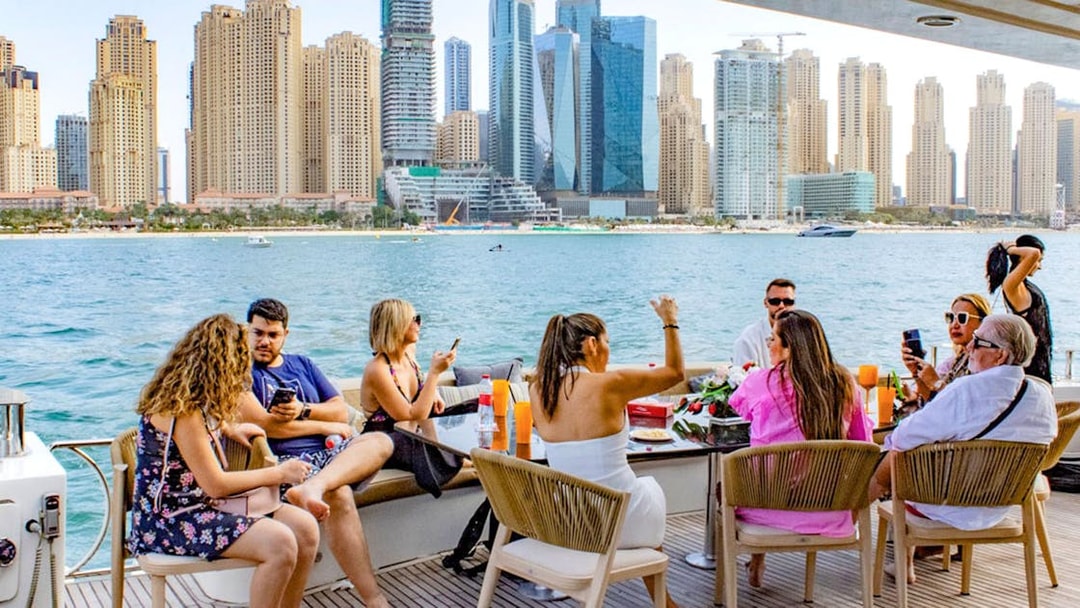 Tourists enjoying a Superyacht TriDeck cruise with Dubai skyline in the background.
