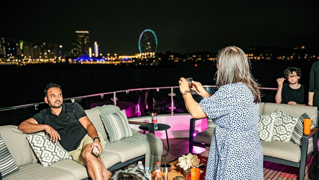 Tourists capturing night views on Superyacht TriDeck Cruise with city skyline.