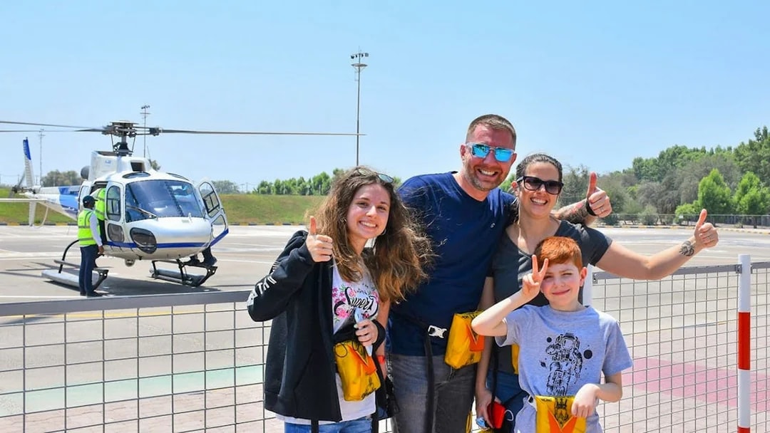 Family posing in front of a helicopter at a helipad in Dubai.