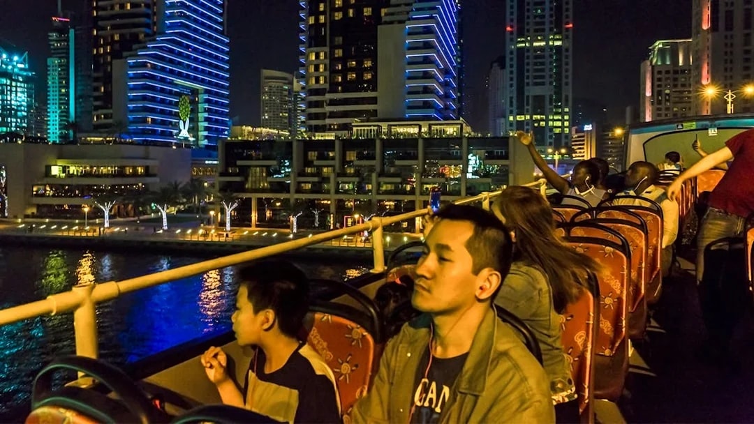 Open-top bus tour at night in Dubai Marina with illuminated skyscrapers.