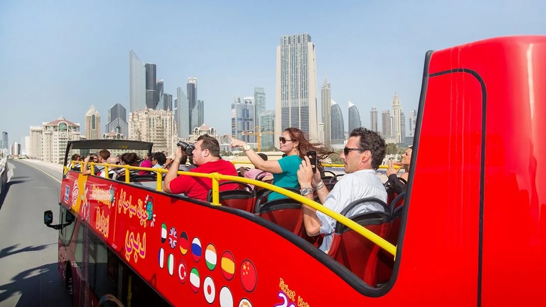 Tourists on a red Citysightseeing bus in Dubai with skyscrapers in the background.