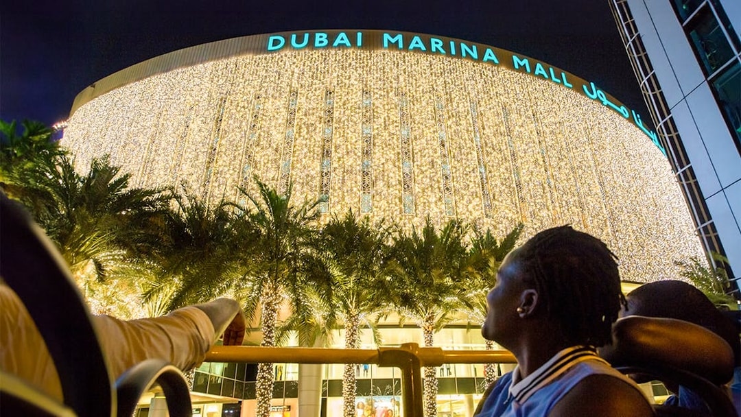 Visitors admire Dubai Marina Mall illuminated at night.