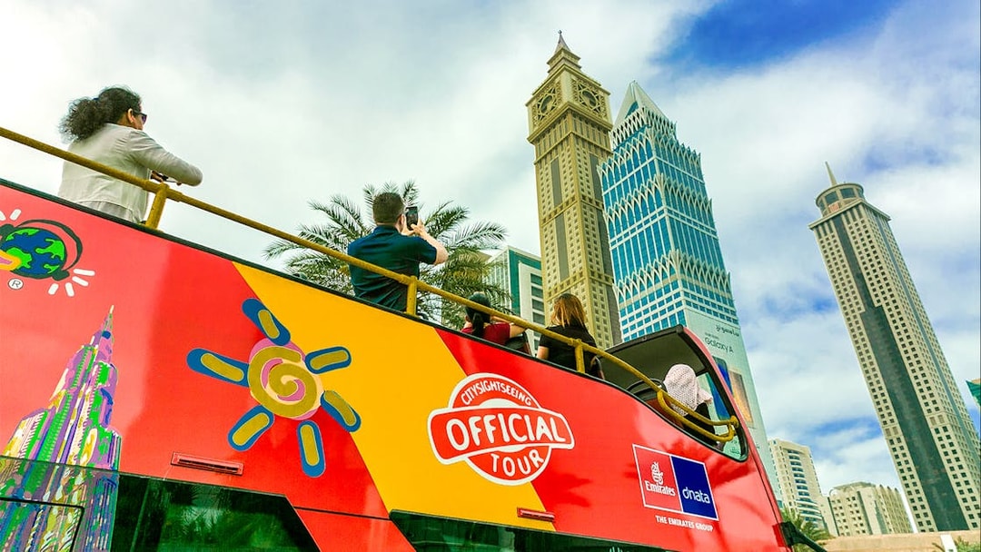 Open-top tour bus with tourists viewing Dubai skyscrapers.