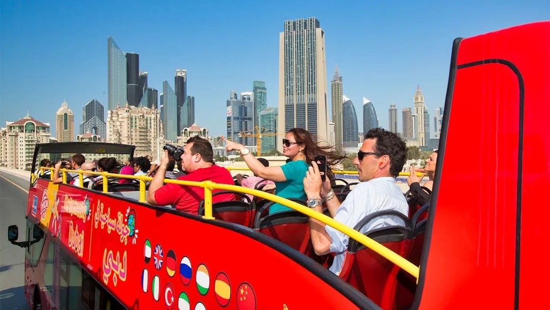 Open-top tour bus with tourists viewing Dubai skyline.