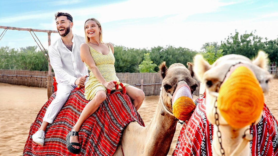 Couple riding camels in desert setting, part of hot air balloon tour with breakfast and quad biking.