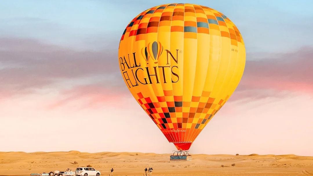 Hot air balloon in desert landscape with vehicles and people preparing for flight.