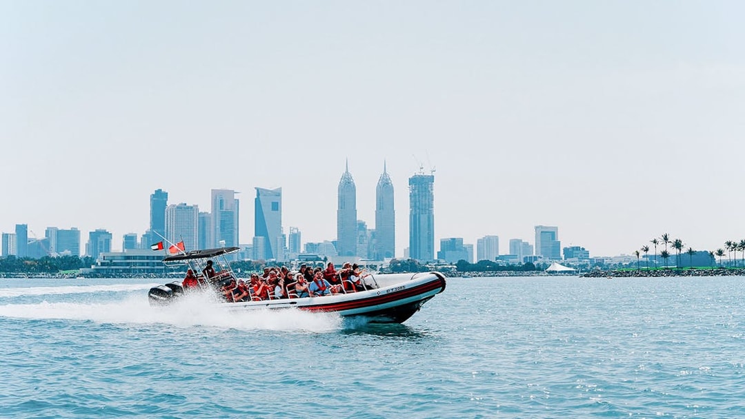 Speedboat with tourists in Dubai Marina, city skyline in background.