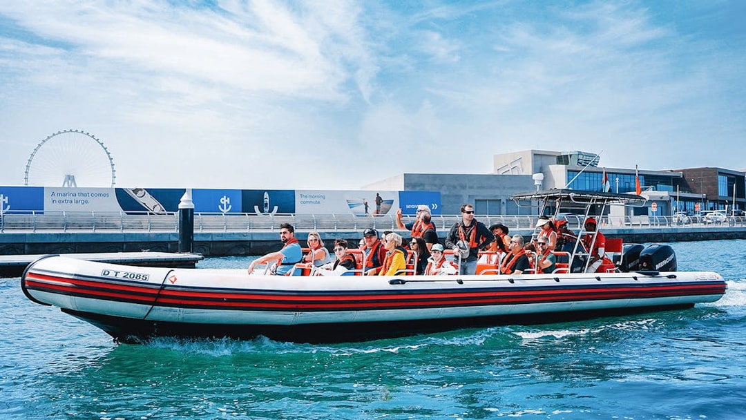 Speedboat with tourists on Dubai Marina tour, passing by waterfront attractions.