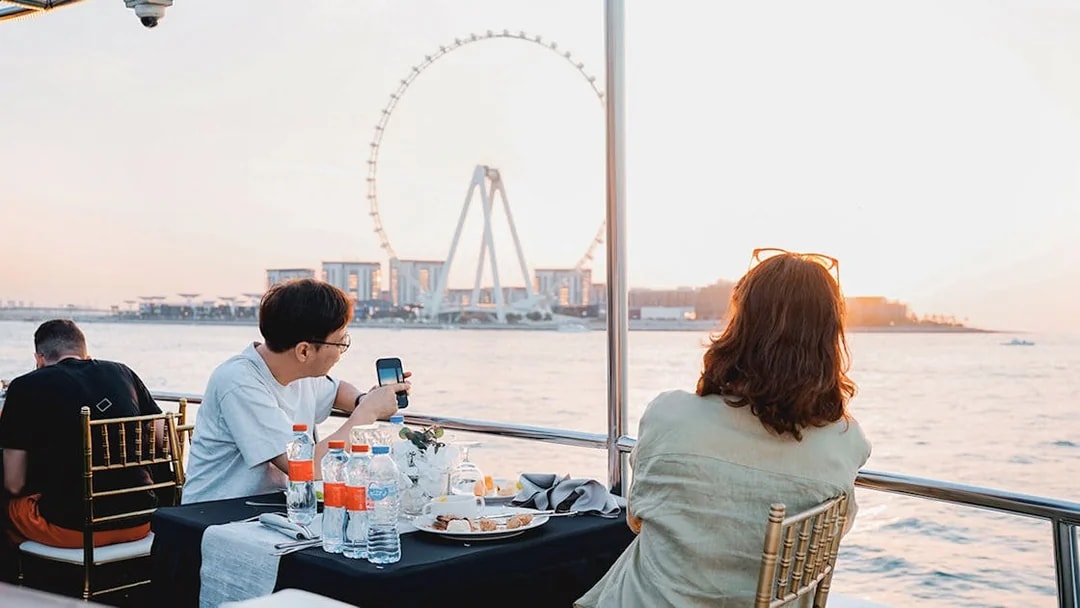 Guests dining on a sunset cruise in Dubai Marina with Ferris wheel view.