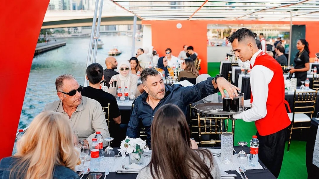 Guests dining on a sunset cruise in Dubai Marina with a waiter serving drinks.