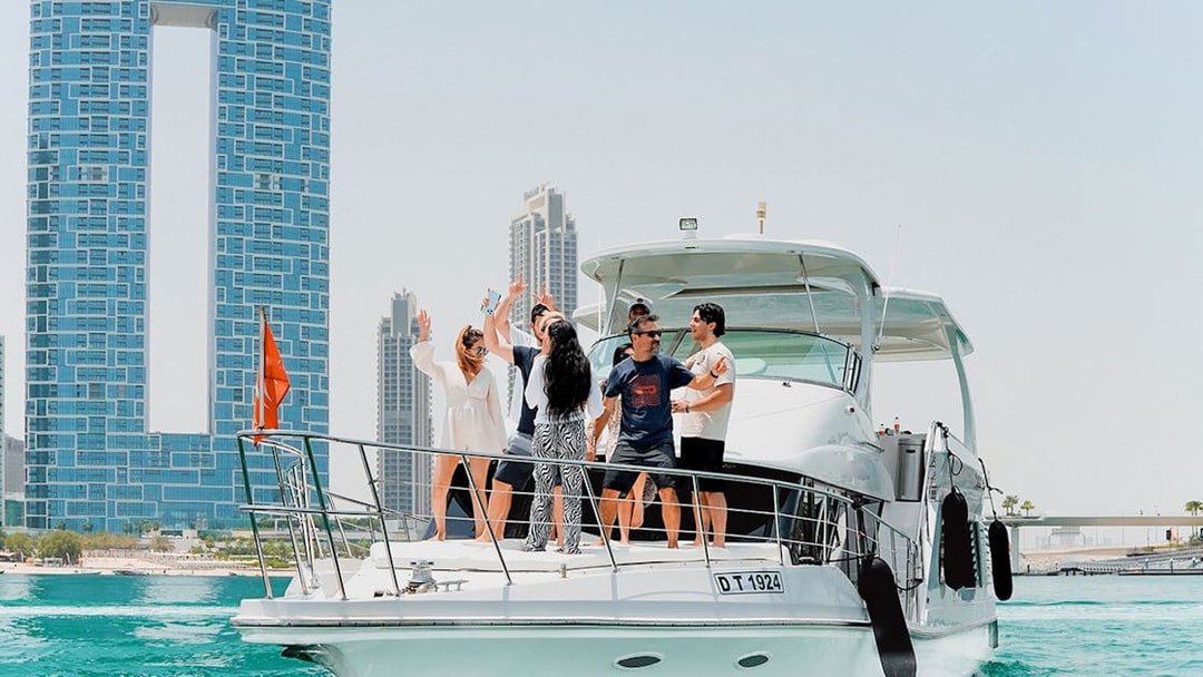 Yacht with people enjoying near JBR, Dubai skyline in background.