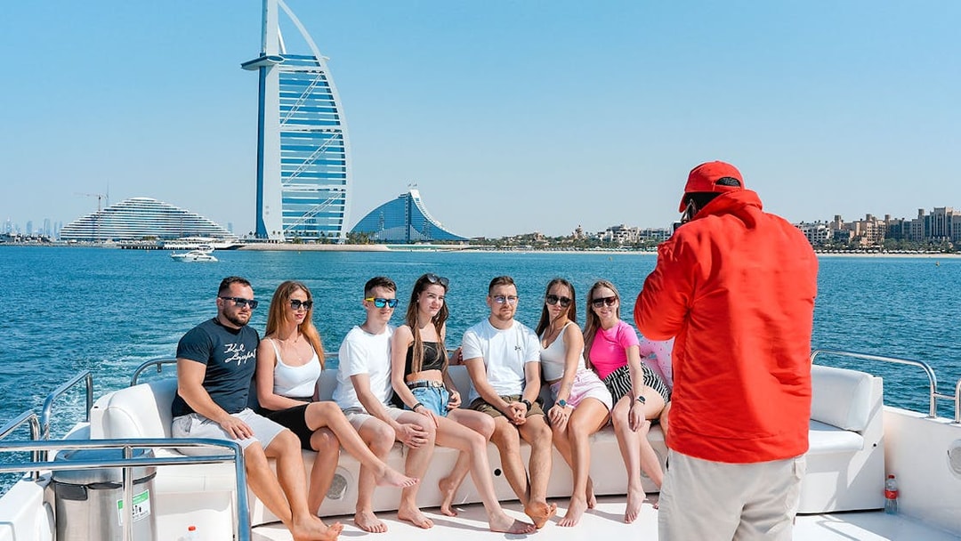 Tourists posing for a photo on a luxury yacht cruise with Burj Al Arab in the background.