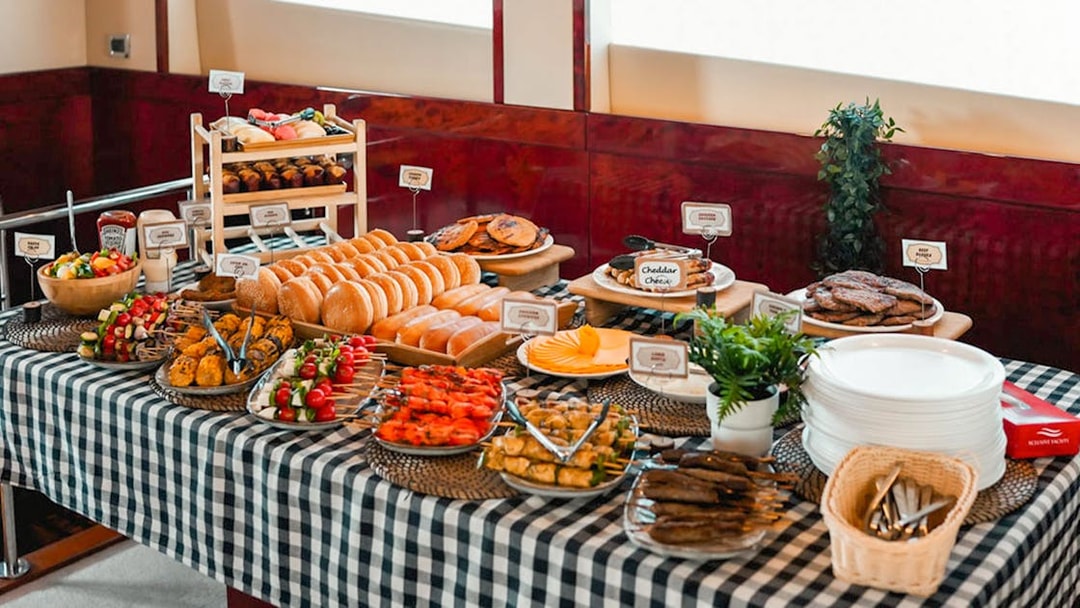 Breakfast buffet on a luxury yacht cruise with assorted pastries, fruits, and skewers.