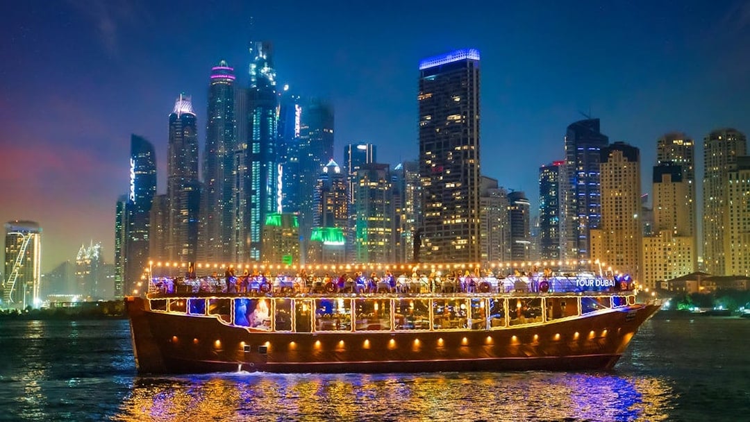 Luxury dhow cruise with lights on Dubai Marina at night, skyscrapers in the background.