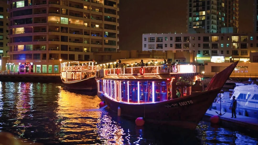 Dhow boats illuminated at night in Dubai Marina during a dinner cruise with live entertainment.