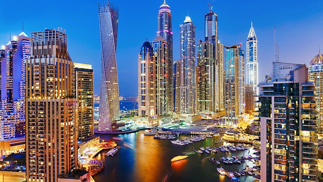 Dubai Marina skyline at night with illuminated skyscrapers and yachts, Combo: Dhow Cruise + Desert Safari.