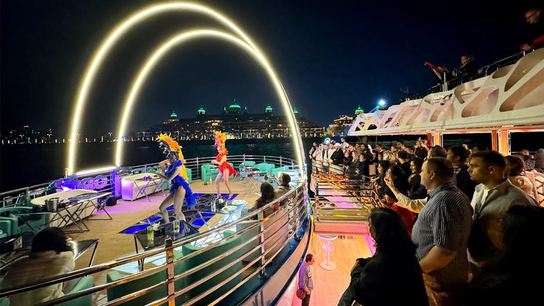 Performers entertaining guests on a cruise ship at night with city lights in the background.