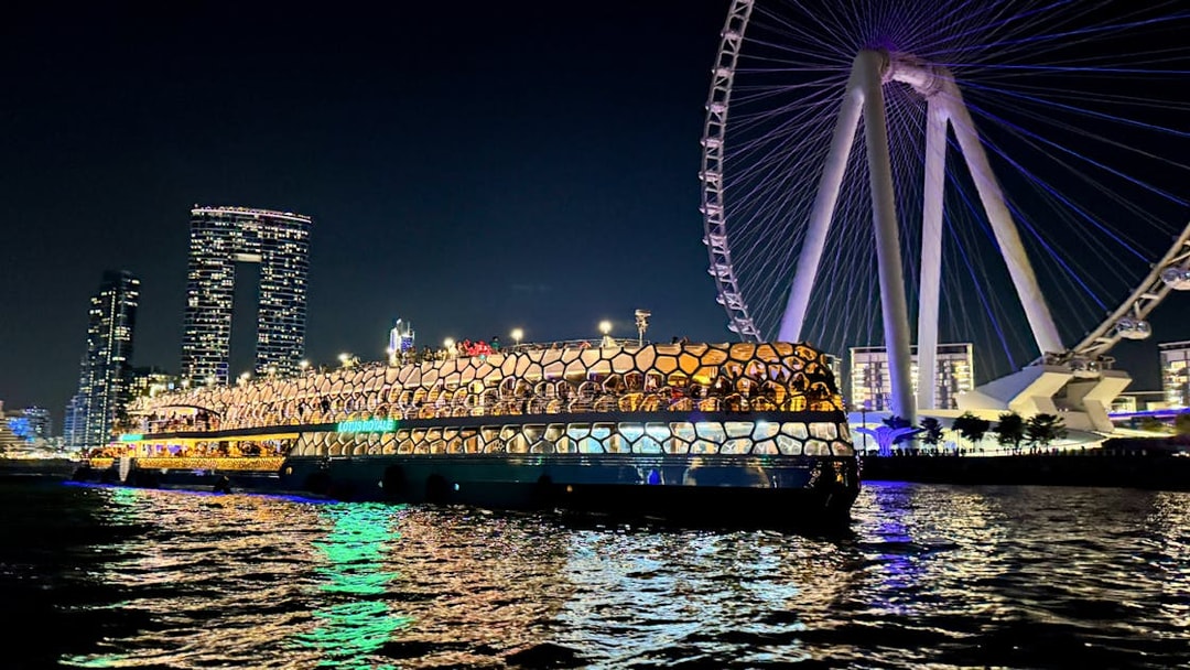 Cruise ship illuminated at night near a large Ferris wheel on the sea.
