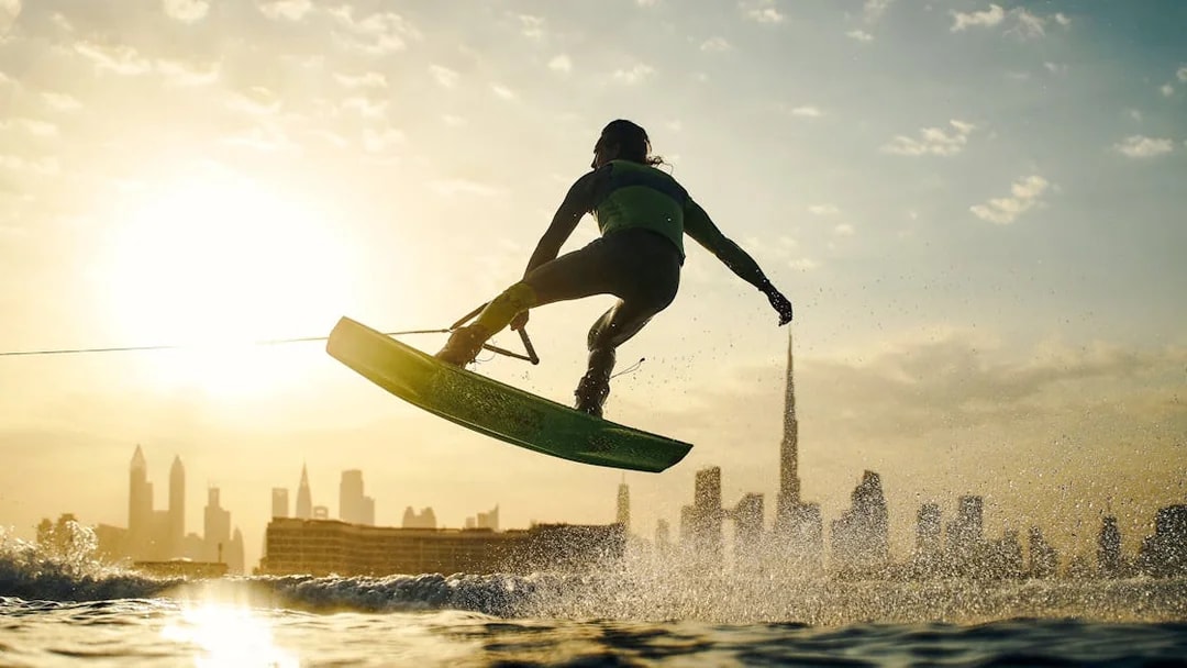 Tourist wakesurfing at sunset with Dubai skyline in background.