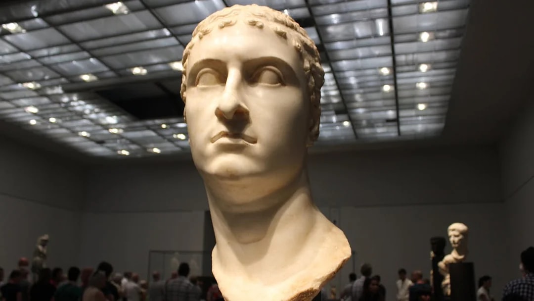 Bust of a Roman figure displayed at Louvre Museum Abu Dhabi with visitors in the background.