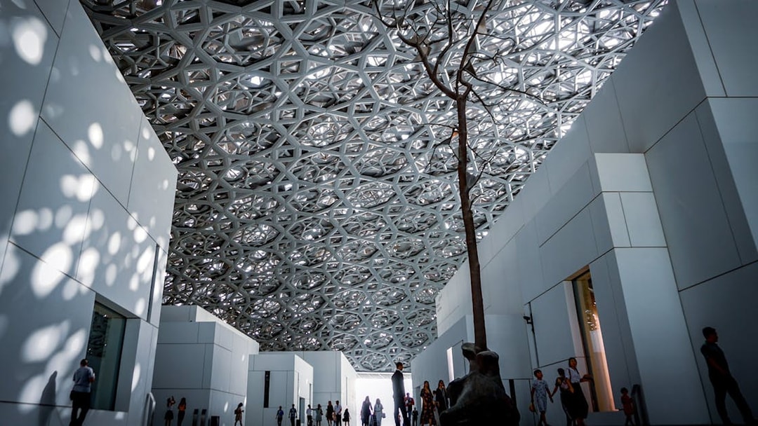 Louvre Abu Dhabi interior with geometric ceiling and visitors walking.