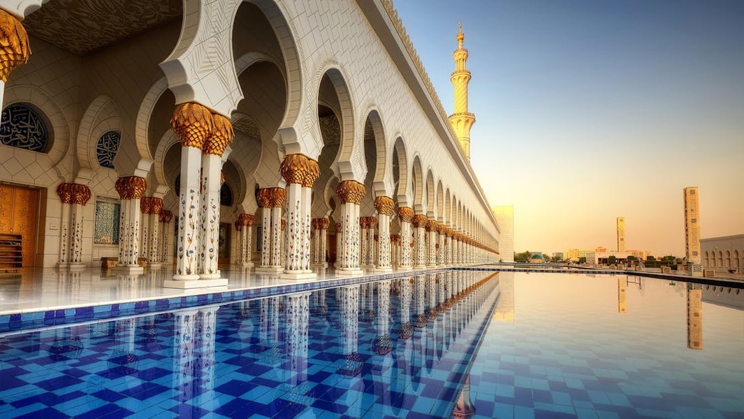 Abu Dhabi Mosque exterior with reflection in water, part of guided tour including Louvre Museum.