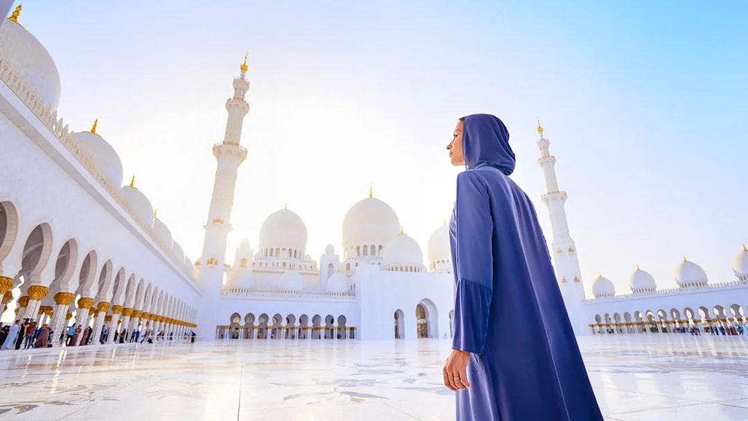 Woman in abaya at Sheikh Zayed Grand Mosque, Abu Dhabi, with domes and minarets in view.