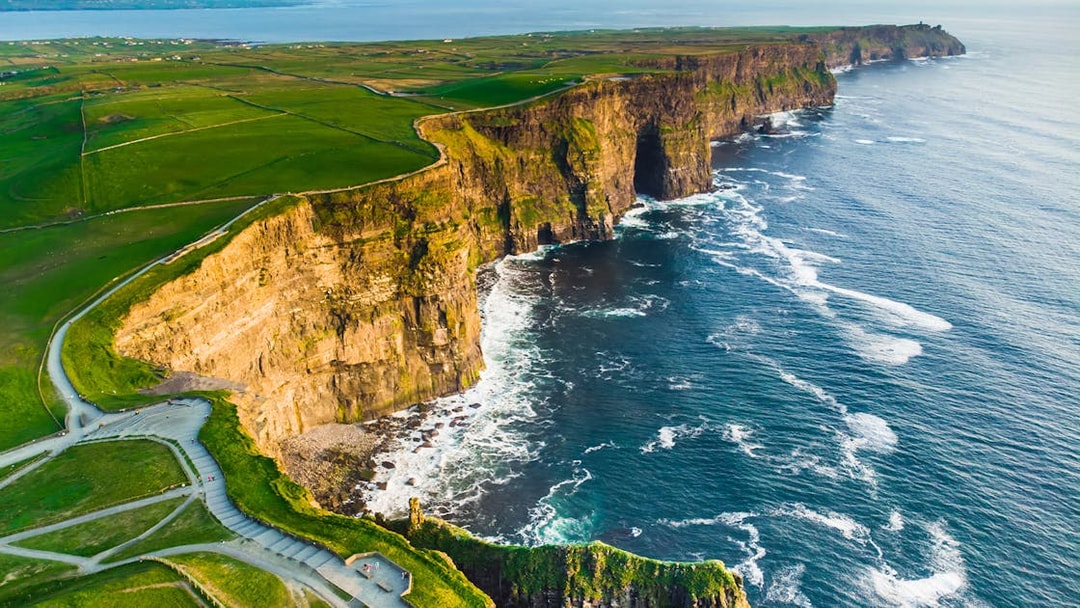 Aerial view of the Cliffs of Moher, Ireland, with waves crashing against the rocky coastline.