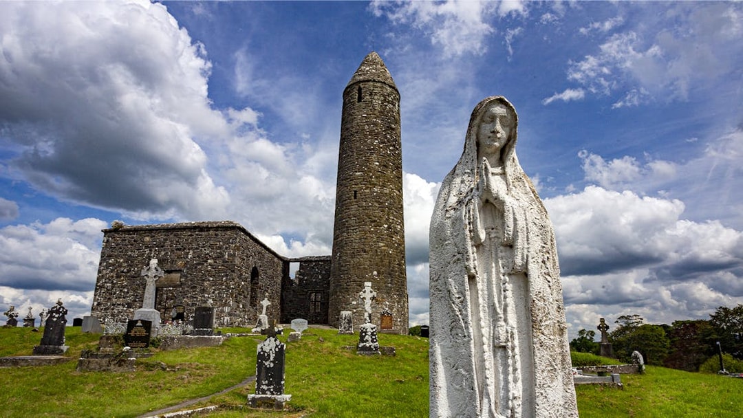 Glendalough Monastic Site with round tower and statue in a historic cemetery.