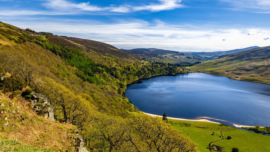 Wicklow Mountains view with lush greenery and a serene lake under a blue sky.