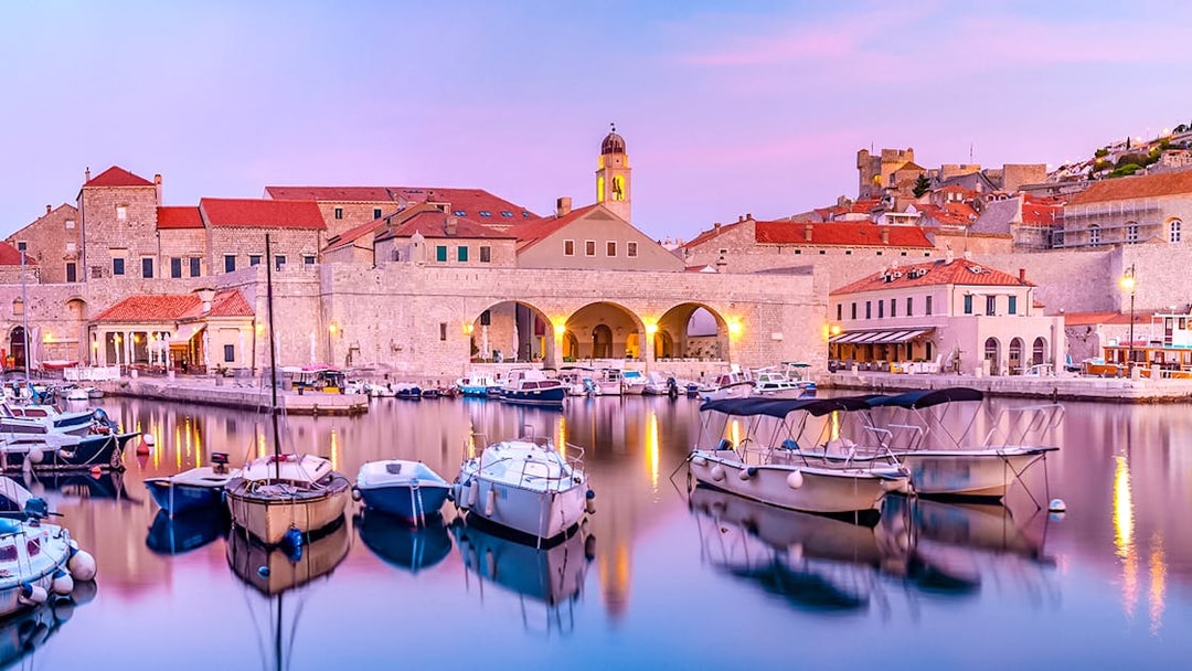 Dubrovnik old town harbor at sunset with boats and historic buildings.