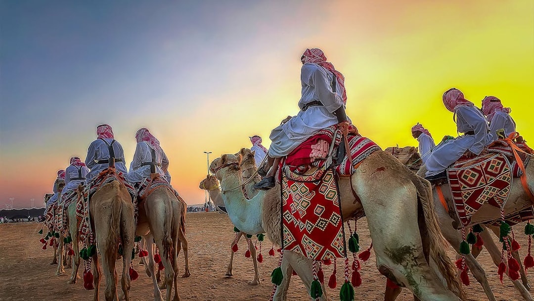 Camels with riders in traditional attire at sunset, Dubai desert safari.