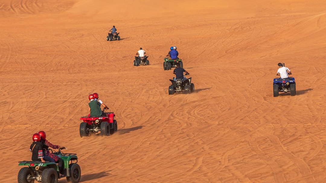 People riding quad bikes on sand dunes during a desert safari in Dubai.