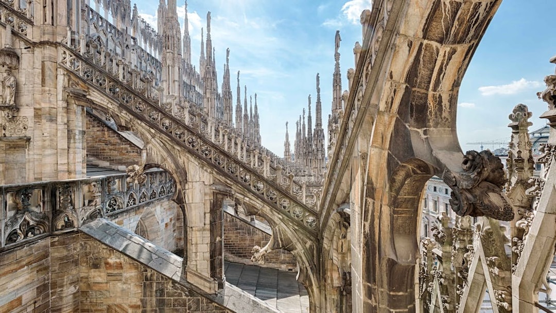 Duomo Milan rooftops with intricate spires and stone carvings under a clear sky.