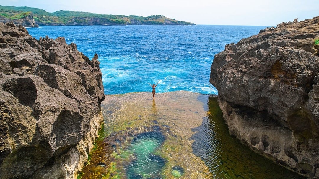 Tourist standing on a cliff at West Nusa Penida Island, overlooking the ocean.
