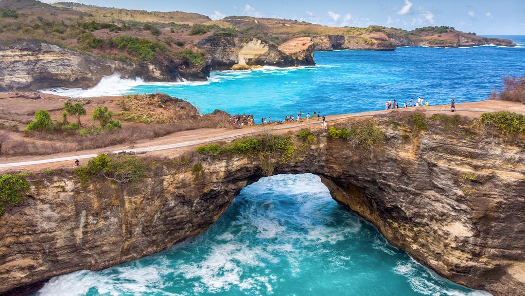 Tourists on a cliff at Broken Beach, West Nusa Penida, Indonesia, overlooking turquoise waters.