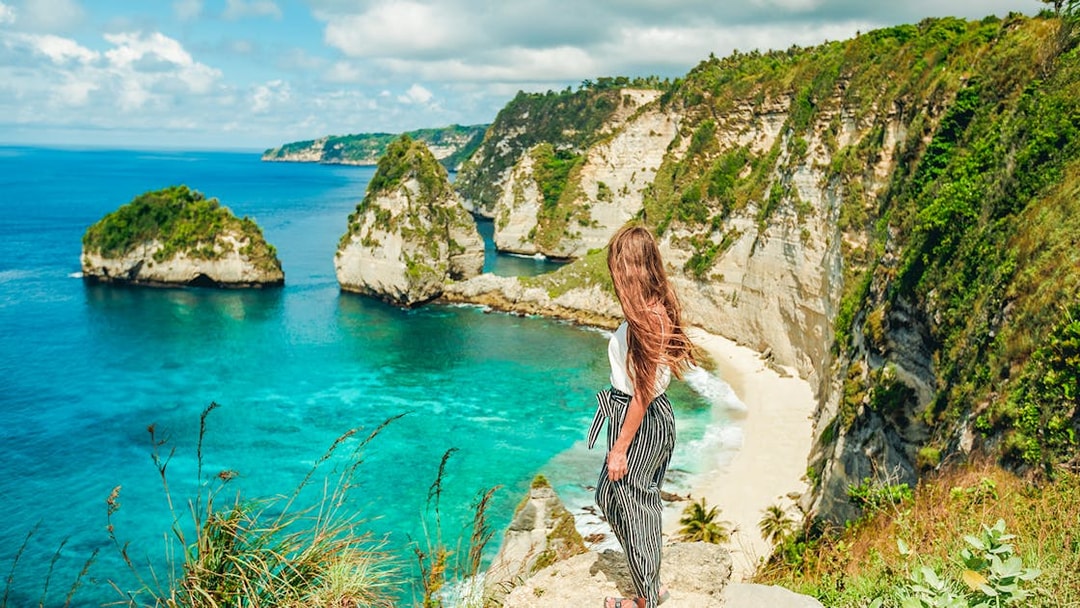 Woman overlooking cliffs and ocean on Nusa Penida Island tour, Indonesia.