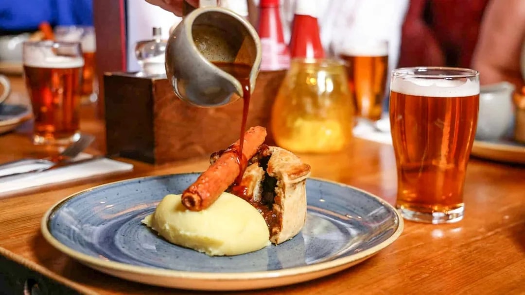 Pouring gravy over pie and mash with a pint of beer on the Eating London food tour.