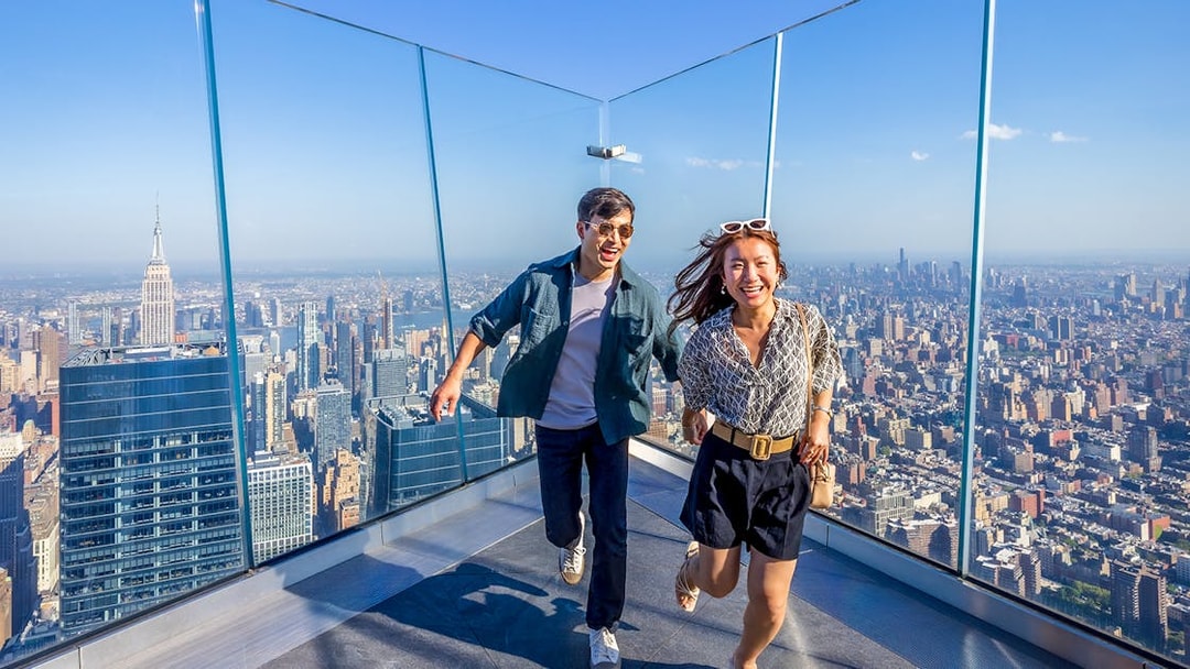 Visitors enjoying the view from an observation deck in New York City with the Empire State Building in the background.