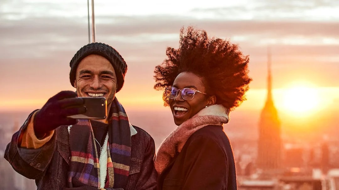 Couple taking a selfie on the Sky Deck with city skyline at sunset.
