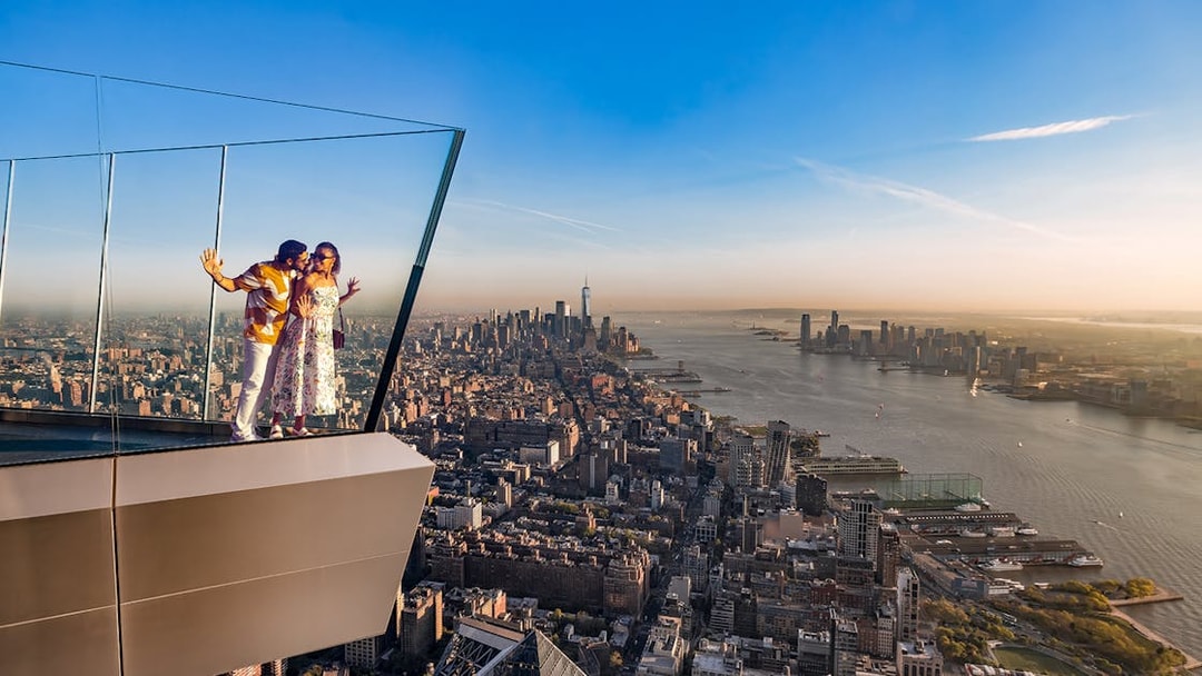 Couple enjoying view from the western overhang of the Edge Observation Deck, New York City skyline in background.