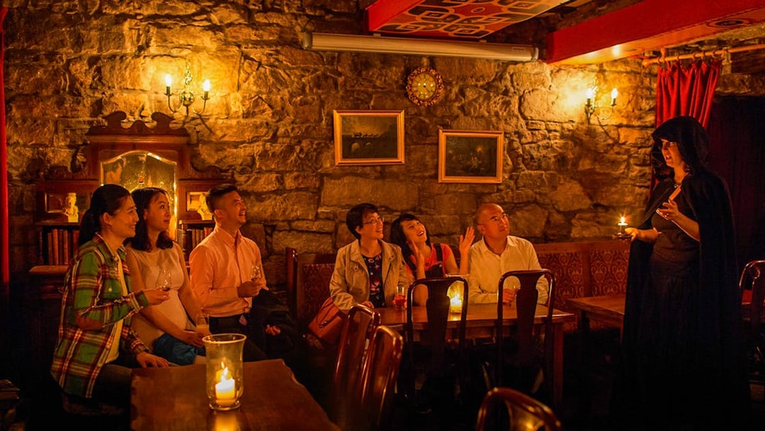 Group listening to a storyteller in a dimly lit Edinburgh pub during ghost tour.