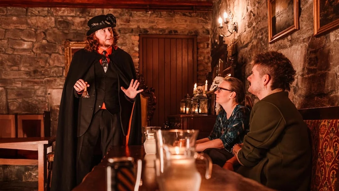 Tour guide in period costume leading an evening underground ghost tour in Edinburgh.