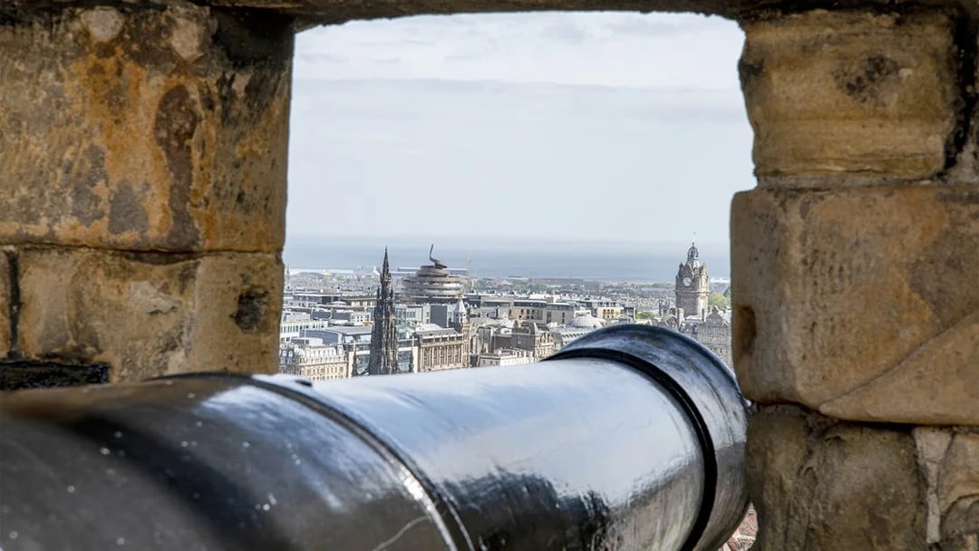 Cannon view from Edinburgh Castle overlooking cityscape and sea.