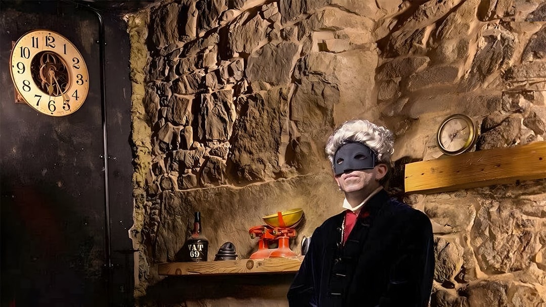 Masked figure in historical attire in a dimly lit stone room, part of Extreme Paranormal Activity Tour.