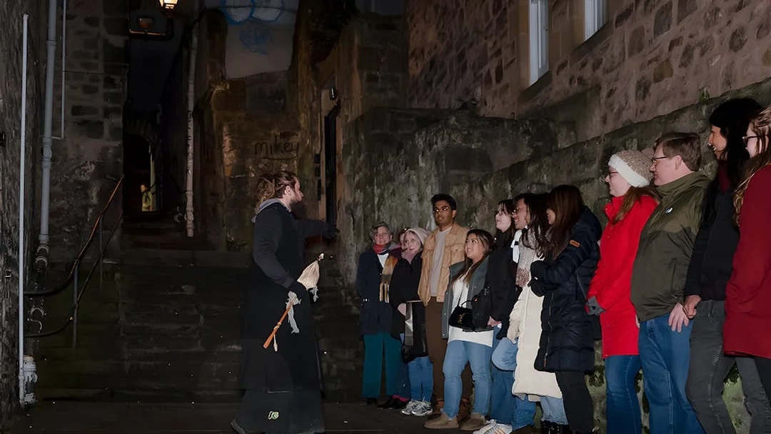 Tour guide leading a group on an Extreme Paranormal Activity Tour in a dimly lit alley.