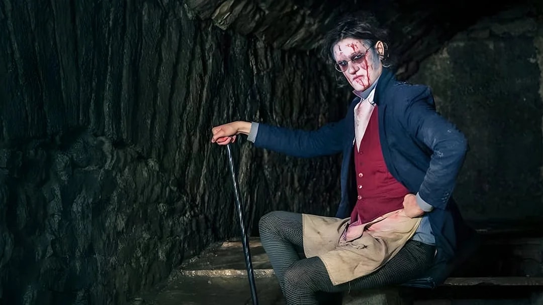 Victorian-era actor in makeup and costume in a dimly lit underground setting for paranormal tour.