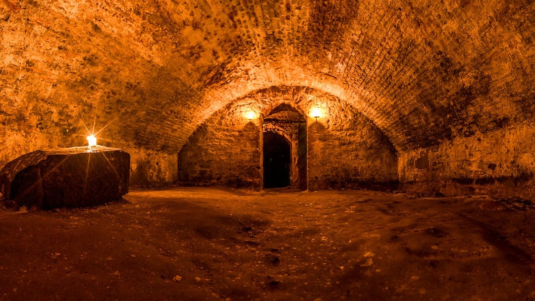 Scottish underground dungeon with stone walls and candlelit archway.