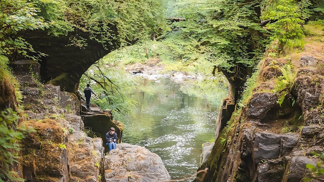 Visitors exploring a lush green gorge with a river on the Whisky & Waterfalls Day Tour from Edinburgh.