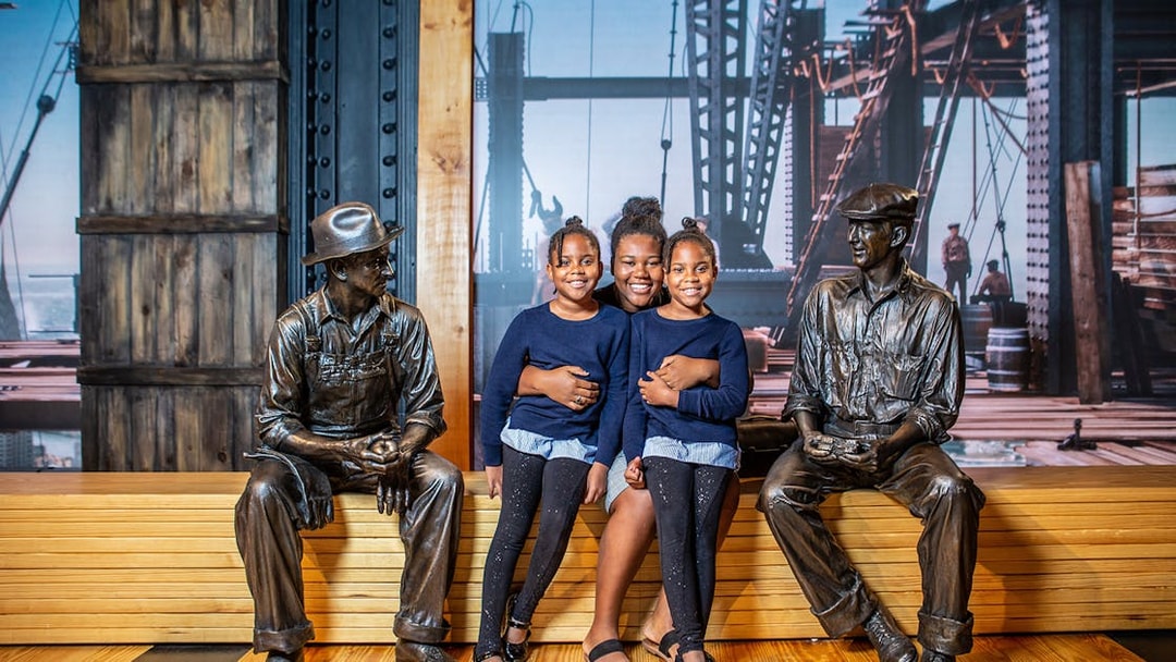 Family posing with construction worker statues at museum exhibit.